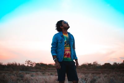 Young man standing on field against sky during sunset