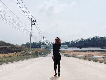 Rear view of woman standing on road against sky