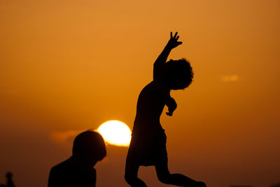 Silhouette people against orange sky during sunset