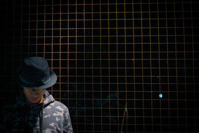 Man in hat standing against fence 