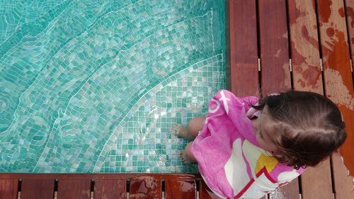 High angle view of girl wrapped in towel sitting at poolside