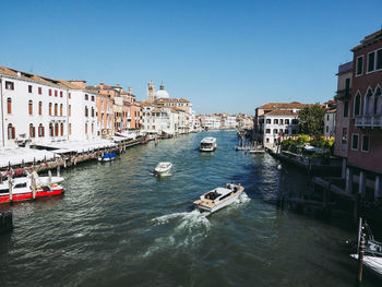 Boats in canal amidst buildings against clear sky