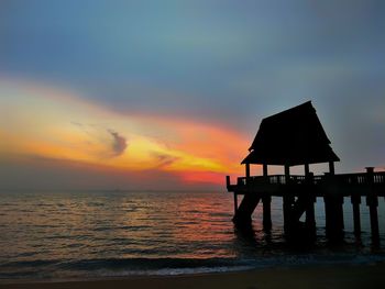 Silhouette lifeguard hut on beach against sky during sunset