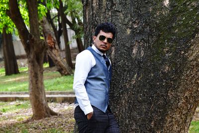 Portrait of young man wearing waistcoat while leaning on tree at park