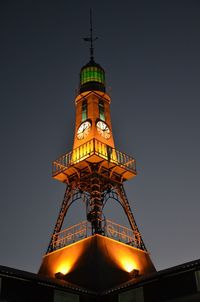 Low angle view of illuminated lighthouse against clear sky at night