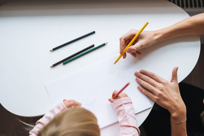 Little girl toddler with her mother drawing with colored pencils on table in children's room at home