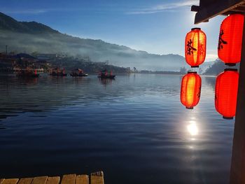 Red lanterns hanging by lake against sky