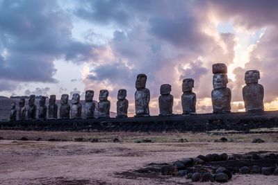 Moai statues against cloudy sky at sunrise