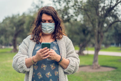 Woman wearing flu mask using smart phone standing at park