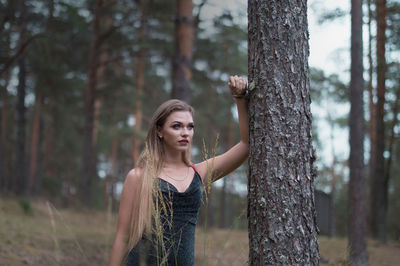 Woman standing by tree trunk in forest