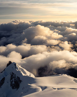 Aerial view of snowcapped mountains against cloudy sky during sunset