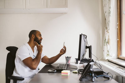 Male doctor consulting on video call through smart phone while sitting at desk