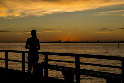 Rear view of silhouette woman standing on pier against sky during sunset
