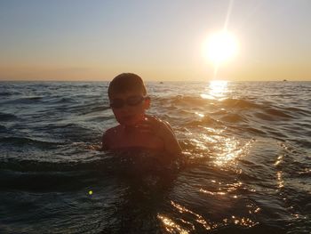 Man in sea against sky during sunset