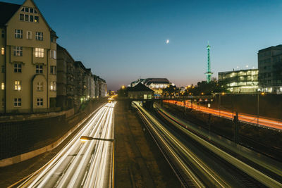 Light trails on street amidst buildings against sky at dusk