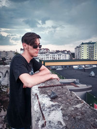 Young man wearing sunglasses standing by cityscape against sky
