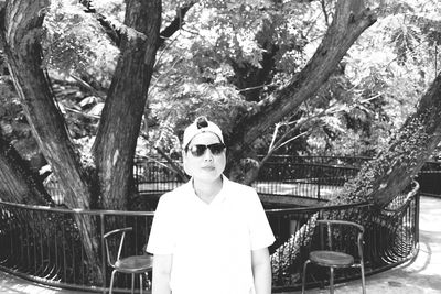 Portrait of woman wearing sunglasses and cap against tree