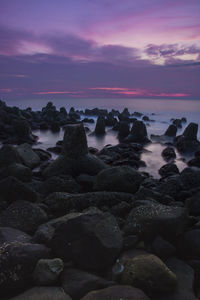 Rocks on beach against sky during sunset