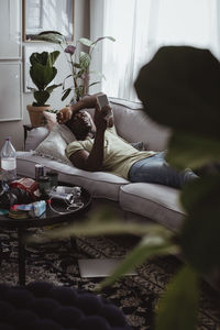 Sad man using smart phone while lying on sofa at home