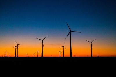 Silhouette wind turbines on field against sky during sunset