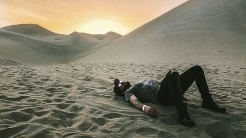 Man lying down on sand at beach against sky during sunset