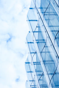 Detail of the wavy glass curtain wall facade of a nice modern building, sky and clouds reflecting