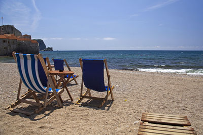 Deck chairs on beach against sky