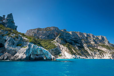 Rock formations in sea against clear blue sky