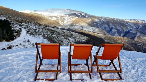 Deck chairs on snow covered mountain against sky