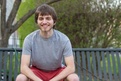 Portrait of a smiling young man sitting on railing