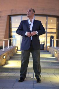 Businessman buttoning blazer while standing against building