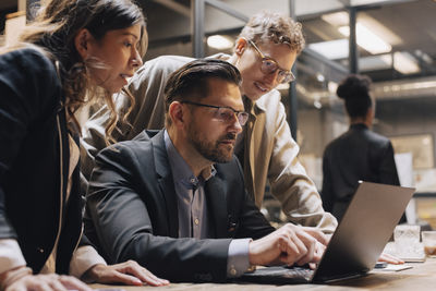 Mature male manager discussing over laptop with businessman and businesswoman at office