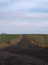 Empty road amidst field against sky