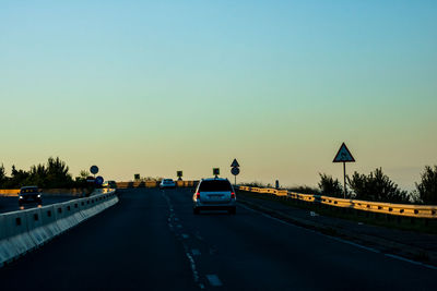 Cars on road against clear sky during sunset