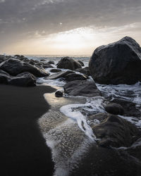 Rocks in sea against sky during sunset