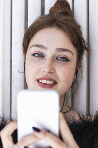 Beautiful woman with blue eyes holding smart phone while listening music on bench