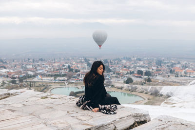 Woman sitting against buildings in city against sky