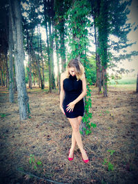 Young woman standing by tree in forest