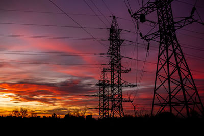 Low angle view of silhouette electricity pylon against dramatic sky