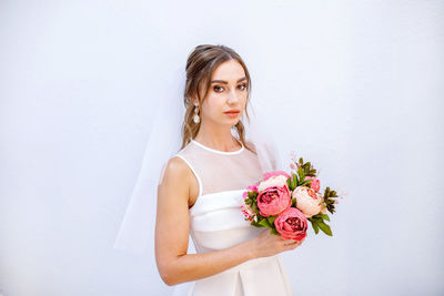 Young woman holding red rose against white wall