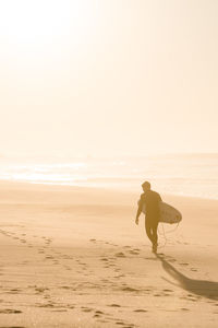 Silhouette man carrying surfboard at beach during sunset