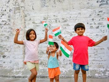 Portrait of happy children with indian flags standing against wall