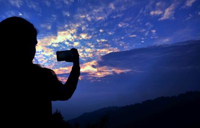 Rear view of silhouette person photographing at sunset
