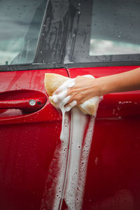 Hands holding a sponge, washing a car with soap.