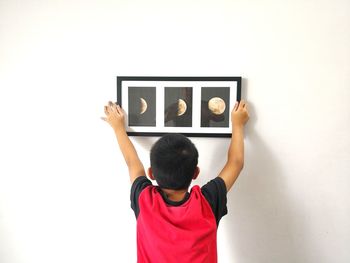 Rear view of boy adjusting picture frame on white wall