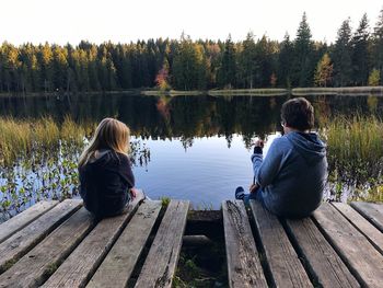 Rear view of siblings sitting by lake on pier