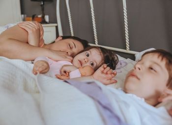 Mother sleeping with son and daughter on bed at home