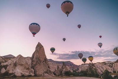 Low angle view of hot air balloons flying over landscape against sky during sunset