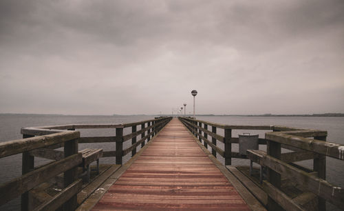 Empty jetty leading to pier over sea against sky