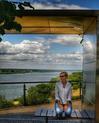 Full length portrait of smiling man sitting against sky